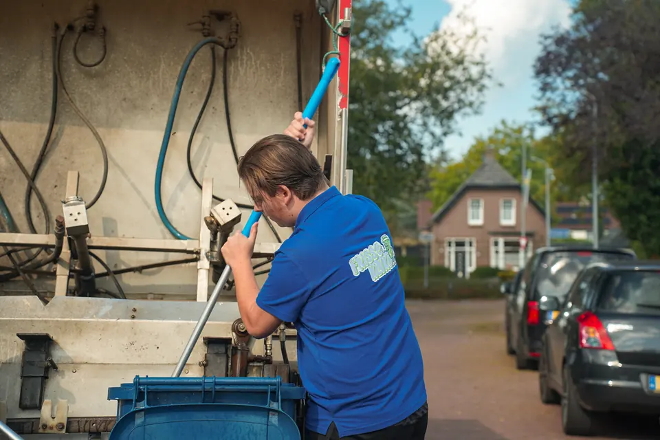 Medewerker borstelt de binnenkant van een blauwe container bij de reinigingswagen.
